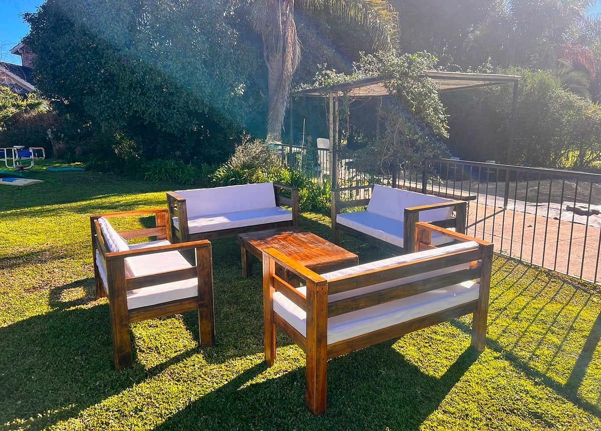 Living exterior de madera con almohadones blancos sobre pasto